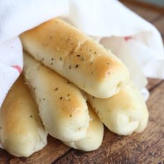 some bread sticks are sitting on top of a wooden table and wrapped in a white towel