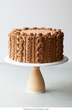 a chocolate cake sitting on top of a white cake platter next to a wooden spatula