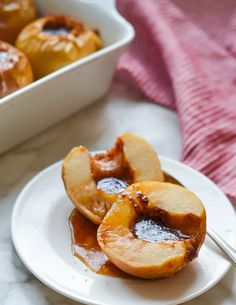 baked apples with caramel sauce on a white plate next to a baking dish and pink towel