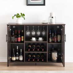 a wooden cabinet with wine bottles and glasses on it in front of a white wall