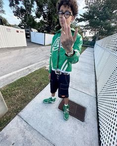 a young boy making the peace sign with his hand while wearing green shoes and shorts