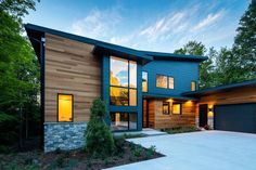 a modern home with wood and stone accents in the evening light, surrounded by trees