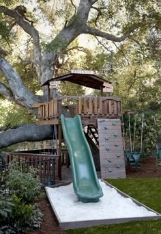 a green slide in the middle of a yard next to a tree and some bushes