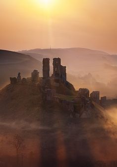 an old castle sits on top of a hill in the foggy countryside at sunset