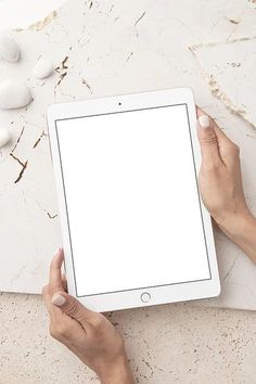 two hands holding an ipad with a white screen on top of it and some rocks in the background