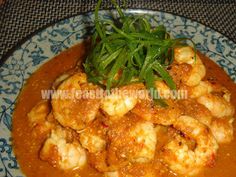 a blue and white plate topped with shrimp covered in sauce, garnished with green leaves