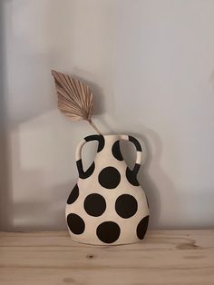 a black and white polka dot vase sitting on top of a wooden table next to a plant