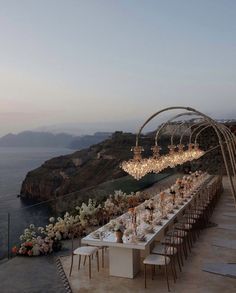 an outdoor dining area overlooking the ocean with chandeliers hanging from it's ceiling