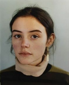 a woman with brown hair wearing a turtle neck sweater and earrings looking at the camera