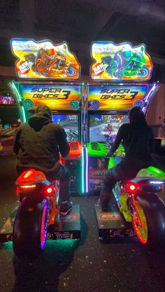 two people riding motorcycles with neon lights on the back and front seats in an arcade