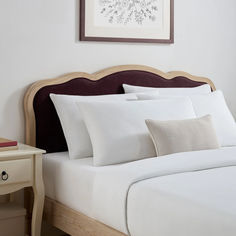 a bed with white sheets and pillows next to a painting on the wall above it