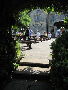 people are sitting on benches in front of an old stone building with ivy growing around it