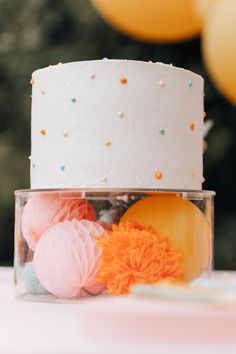 a white cake sitting on top of a table next to balloons and confetti