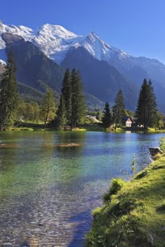 a lake surrounded by mountains and trees in the foreground with a house on the other side