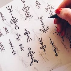 a woman's hand writing on a piece of paper with various symbols drawn on it