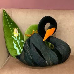 a stuffed duck sitting on top of a couch next to a green leaf