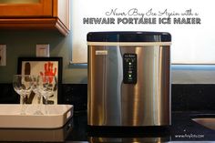 a stainless steel ice maker sitting on top of a kitchen counter next to wine glasses