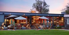 an outdoor patio with chairs and umbrellas on the grass at sunset or dawn in front of a building