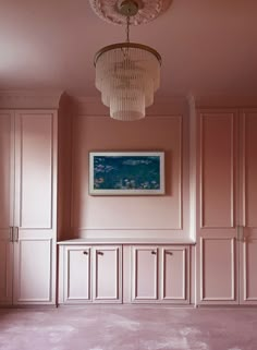 an empty room with pink walls and white cupboards in the corner, there is a chandelier hanging from the ceiling