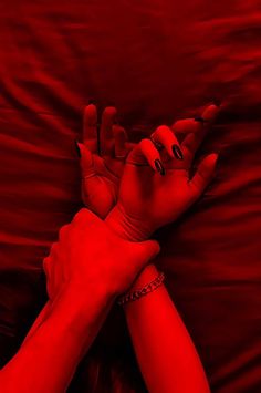 two hands reaching out to each other on a red sheet covered bed with the sheets pulled back