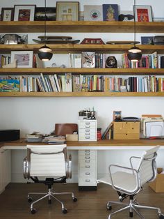 two white office chairs sitting in front of a desk with bookshelves above it