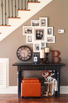 a black table topped with pictures and an orange suitcase next to a stair case filled with photos