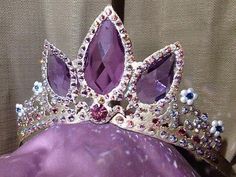 a tiara is shown on top of a purple dress with pearls and jewels around it