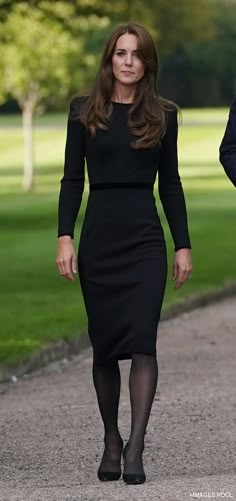 a woman in a black dress walking down a path