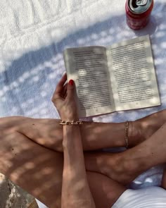 a woman laying on the ground reading a book and drinking a beverage in her hand