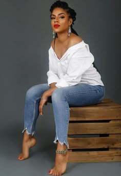 a woman sitting on top of a wooden crate wearing jeans and a white off the shoulder shirt