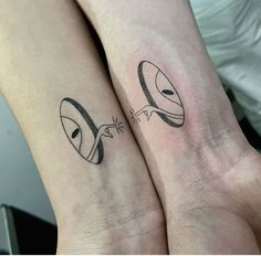 two people with matching tattoos on their arms, one has an alien face and the other has