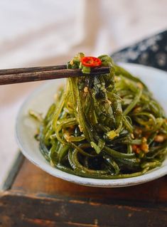 a white bowl filled with green beans and chopsticks on top of a wooden table