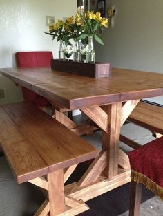 a wooden table with two benches next to it and flowers in a vase on top