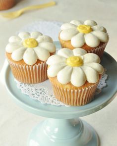 three cupcakes with white frosting and yellow centers on a blue cake plate