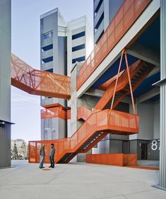 two men are standing in front of an orange staircase that is going up the side of a building