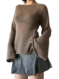 a woman wearing a brown sweater and pleated skirt with her hands in her pockets