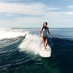 a woman riding a surfboard on top of a wave in the ocean, wearing a white swimsuit