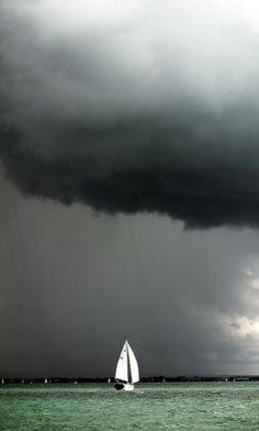 a sailboat in the ocean under a stormy sky with dark clouds above it and green water below