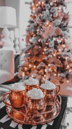 three copper mugs sitting on a tray in front of a christmas tree