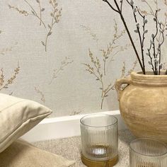 a vase and two glasses sitting on the floor in front of a wallpapered wall