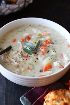 a white bowl filled with chicken and vegetable soup next to two biscuits on a table