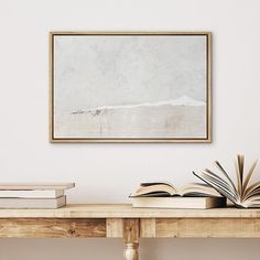 an open book sitting on top of a wooden table in front of a framed painting