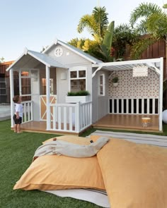 a little boy standing in front of a small house on the grass with a bed