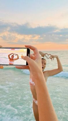 a woman taking a selfie with her cell phone at the beach while sun is setting