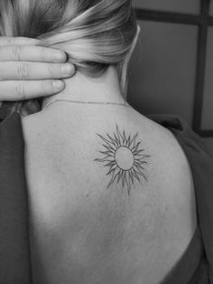 the back of a woman's shoulder with a small sun tattoo on her upper arm