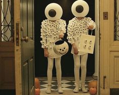 two people dressed up in white holding pumpkins and looking at each other through an open door