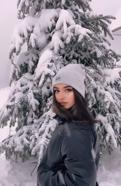 a woman standing in front of a snow covered tree with her hands on her hips