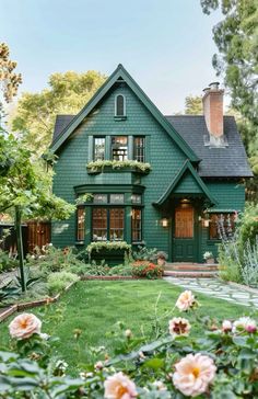 a green house with lots of windows and flowers in the front yard, surrounded by greenery