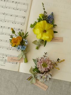 three boutonnieres with flowers on top of sheet music