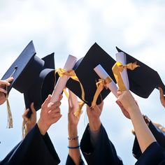 four graduates in black caps and gowns hold up their mortars with yellow ribbons